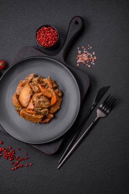 Lezzetli sebze güveci, patates, sığır eti, mantar, havuç, tuz, baharat ve otlar koyu beton arka planda.