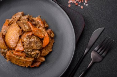 Lezzetli sebze güveci, patates, sığır eti, mantar, havuç, tuz, baharat ve otlar koyu beton arka planda.