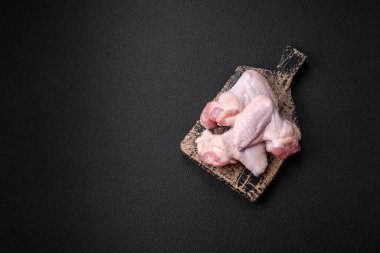 Taze çiğ tavuk kanatları. Tuz ve baharatlarla. Koyu beton bir arka planda pişirmeye hazır.