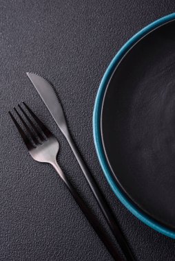 Beton zeminde güzel, boş, seramik bir tabak. Masada yemek servisi için mutfak gereçleri