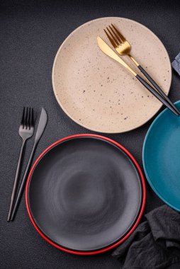 Beton zeminde güzel, boş, seramik bir tabak. Masada yemek servisi için mutfak gereçleri