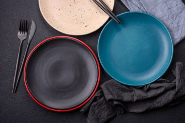 Beton zeminde güzel, boş, seramik bir tabak. Masada yemek servisi için mutfak gereçleri