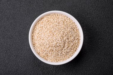 Çiğ beyaz susam tohumu ya da çimento arkaplanındaki bir kasedeki tahıllar. Asya mutfağını hazırlamak için gerekli malzemeler