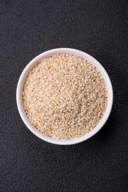 Çiğ beyaz susam tohumu ya da çimento arkaplanındaki bir kasedeki tahıllar. Asya mutfağını hazırlamak için gerekli malzemeler