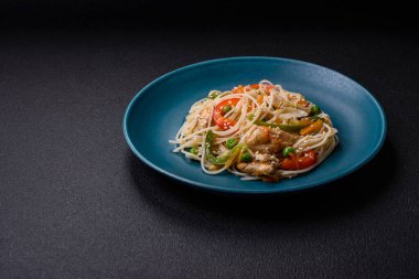 Lezzetli Asya yemekleri pilav eriştesi, tavuk, kuşkonmaz, biber, susam tohumu ve soya sosu ile koyu beton arka planda.