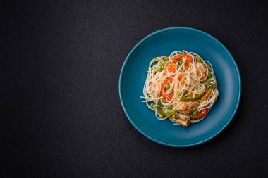 Lezzetli Asya yemekleri pilav eriştesi, tavuk, kuşkonmaz, biber, susam tohumu ve soya sosu ile koyu beton arka planda.