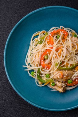 Lezzetli Asya yemekleri pilav eriştesi, tavuk, kuşkonmaz, biber, susam tohumu ve soya sosu ile koyu beton arka planda.