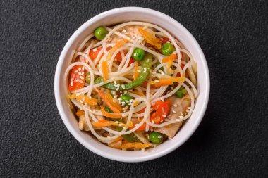 Lezzetli Asya yemekleri pilav eriştesi, tavuk, kuşkonmaz, biber, susam tohumu ve soya sosu ile koyu beton arka planda.