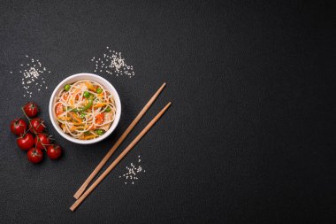 Lezzetli Asya yemekleri pilav eriştesi, tavuk, kuşkonmaz, biber, susam tohumu ve soya sosu ile koyu beton arka planda.