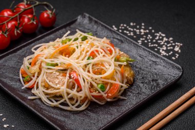 Lezzetli Asya yemekleri pilav eriştesi, tavuk, kuşkonmaz, biber, susam tohumu ve soya sosu ile koyu beton arka planda.