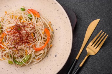 Lezzetli Asya yemekleri pilav eriştesi, tavuk, kuşkonmaz, biber, susam tohumu ve soya sosu ile koyu beton arka planda.