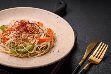 Lezzetli Asya yemekleri pilav eriştesi, tavuk, kuşkonmaz, biber, susam tohumu ve soya sosu ile koyu beton arka planda.