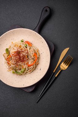 Lezzetli Asya yemekleri pilav eriştesi, tavuk, kuşkonmaz, biber, susam tohumu ve soya sosu ile koyu beton arka planda.