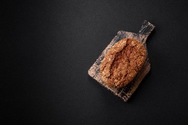 Koyu beton bir arka planda tohumları ve tahılları olan lezzetli çıtır çıtır kahverengi ekmek.