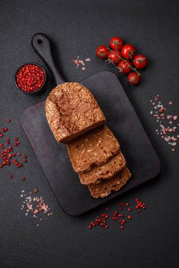 Koyu beton bir arka planda tohumları ve tahılları olan lezzetli çıtır çıtır kahverengi ekmek.