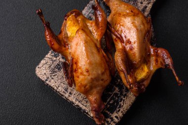 Kavrulmuş bıldırcın, keklik ya da portakalla doldurulmuş koyu beton arka planda baharat ve otlarla dolu güvercin.