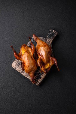 Kavrulmuş bıldırcın, keklik ya da portakalla doldurulmuş koyu beton arka planda baharat ve otlarla dolu güvercin.