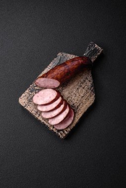 Tuzlu ve baharatlı lezzetli füme sosis koyu beton arka planda dilimler halinde kesilmiş.