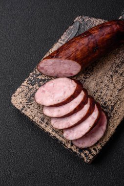 Tuzlu ve baharatlı lezzetli füme sosis koyu beton arka planda dilimler halinde kesilmiş.