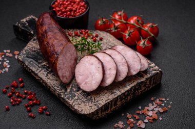 Tuzlu ve baharatlı lezzetli füme sosis koyu beton arka planda dilimler halinde kesilmiş.