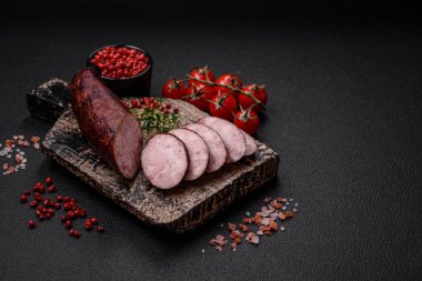 Tuzlu ve baharatlı lezzetli füme sosis koyu beton arka planda dilimler halinde kesilmiş.