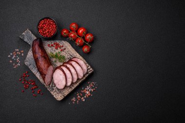 Tuzlu ve baharatlı lezzetli füme sosis koyu beton arka planda dilimler halinde kesilmiş.