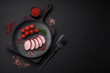 Tuzlu ve baharatlı lezzetli füme sosis koyu beton arka planda dilimler halinde kesilmiş.