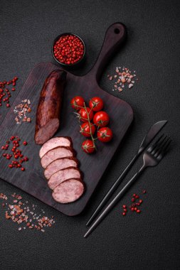 Tuzlu ve baharatlı lezzetli füme sosis koyu beton arka planda dilimler halinde kesilmiş.