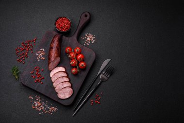 Tuzlu ve baharatlı lezzetli füme sosis koyu beton arka planda dilimler halinde kesilmiş.