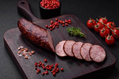 Tuzlu ve baharatlı lezzetli füme sosis koyu beton arka planda dilimler halinde kesilmiş.