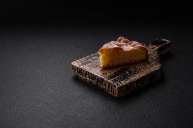 Elma ya da armutla pişirilmiş bir parça ev yapımı turta, üzerine toz serpiştirilmiş, koyu beton bir arka plan.