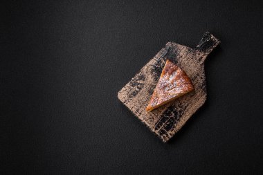 Elma ya da armutla pişirilmiş bir parça ev yapımı turta, üzerine toz serpiştirilmiş, koyu beton bir arka plan.