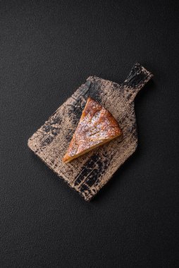 Elma ya da armutla pişirilmiş bir parça ev yapımı turta, üzerine toz serpiştirilmiş, koyu beton bir arka plan.