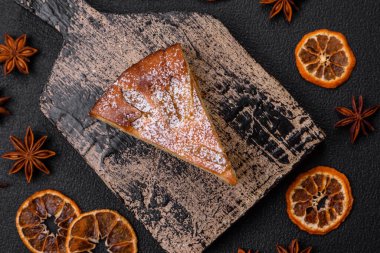 Elma ya da armutla pişirilmiş bir parça ev yapımı turta, üzerine toz serpiştirilmiş, koyu beton bir arka plan.