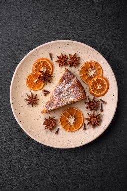 Elma ya da armutla pişirilmiş bir parça ev yapımı turta, üzerine toz serpiştirilmiş, koyu beton bir arka plan.