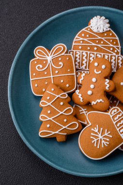 Koyu beton bir masada seramik tabakta farklı renklerde güzel Noel kurabiyeleri.