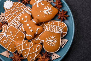 Koyu beton bir masada seramik tabakta farklı renklerde güzel Noel kurabiyeleri.