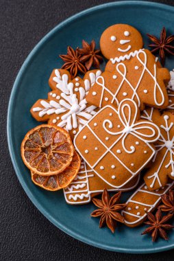 Koyu beton bir masada seramik tabakta farklı renklerde güzel Noel kurabiyeleri.