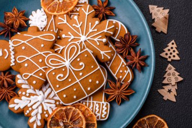 Koyu beton bir masada seramik tabakta farklı renklerde güzel Noel kurabiyeleri.