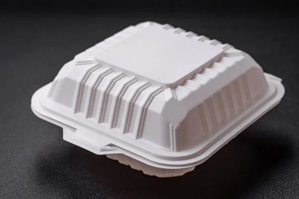 Square plastic or cardboard container of white color for food on a dark concrete background