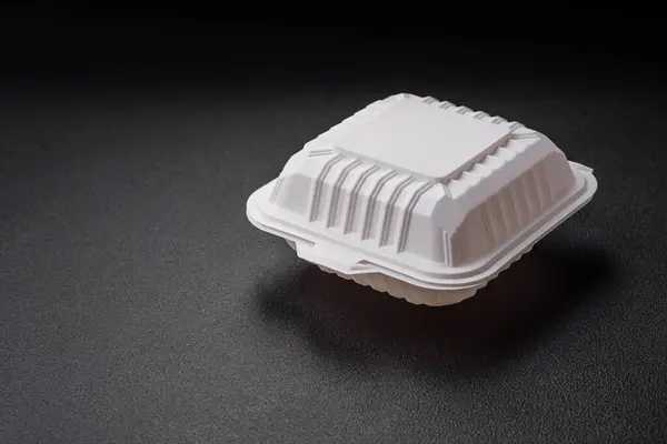 Square plastic or cardboard container of white color for food on a dark concrete background