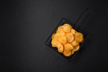 Koyu beton arka planda tuzlu, baharatlı ve otlu patates cipsi.