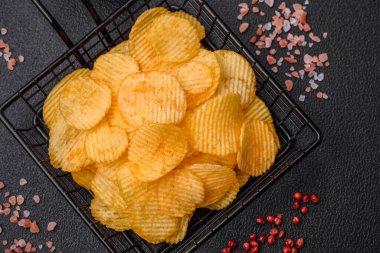 Koyu beton arka planda tuzlu, baharatlı ve otlu patates cipsi.