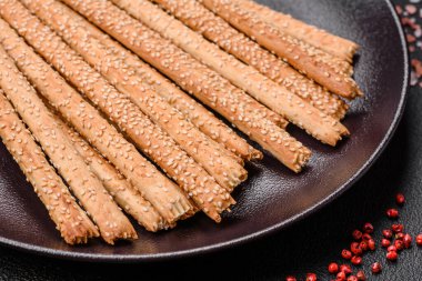 Lezzetli taze Grissini çubukları, koyu beton arka planda tuz ve susam tohumları.