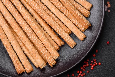 Lezzetli taze Grissini çubukları, koyu beton arka planda tuz ve susam tohumları.