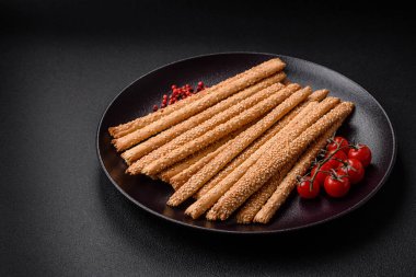 Lezzetli taze Grissini çubukları, koyu beton arka planda tuz ve susam tohumları.