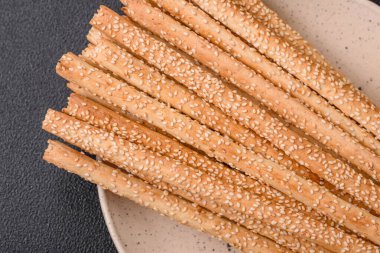 Lezzetli taze Grissini çubukları, koyu beton arka planda tuz ve susam tohumları.