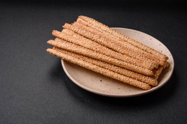 Lezzetli taze Grissini çubukları, koyu beton arka planda tuz ve susam tohumları.