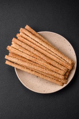 Lezzetli taze Grissini çubukları, koyu beton arka planda tuz ve susam tohumları.