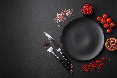 Boş tabak, ahşap kesme tahtası, koyu beton arka planda tuz ve baharatlar.